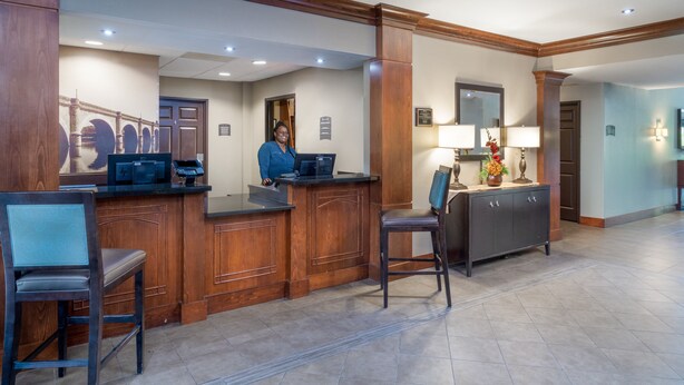A reception area with a wooden reception desk, a computer, and a telephone. There are two chairs and a cabinet with a mirror and a vase of flowers.