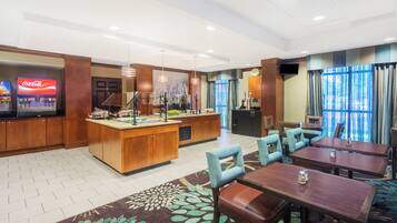 Um saguão de hotel com uma máquina de venda automática de Coca-Cola, uma mesa de recepção e área de estar com mesas e cadeiras.