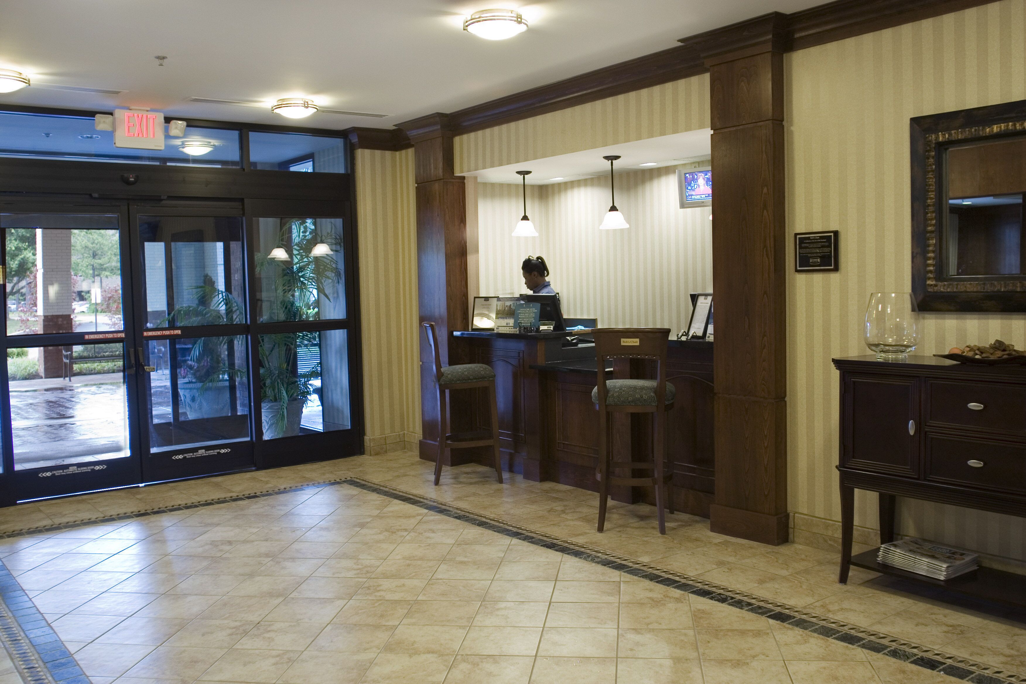 Un vestíbulo de hotel con mostrador de recepción, zona de bar y una puerta señalizada con 'EXIT'.