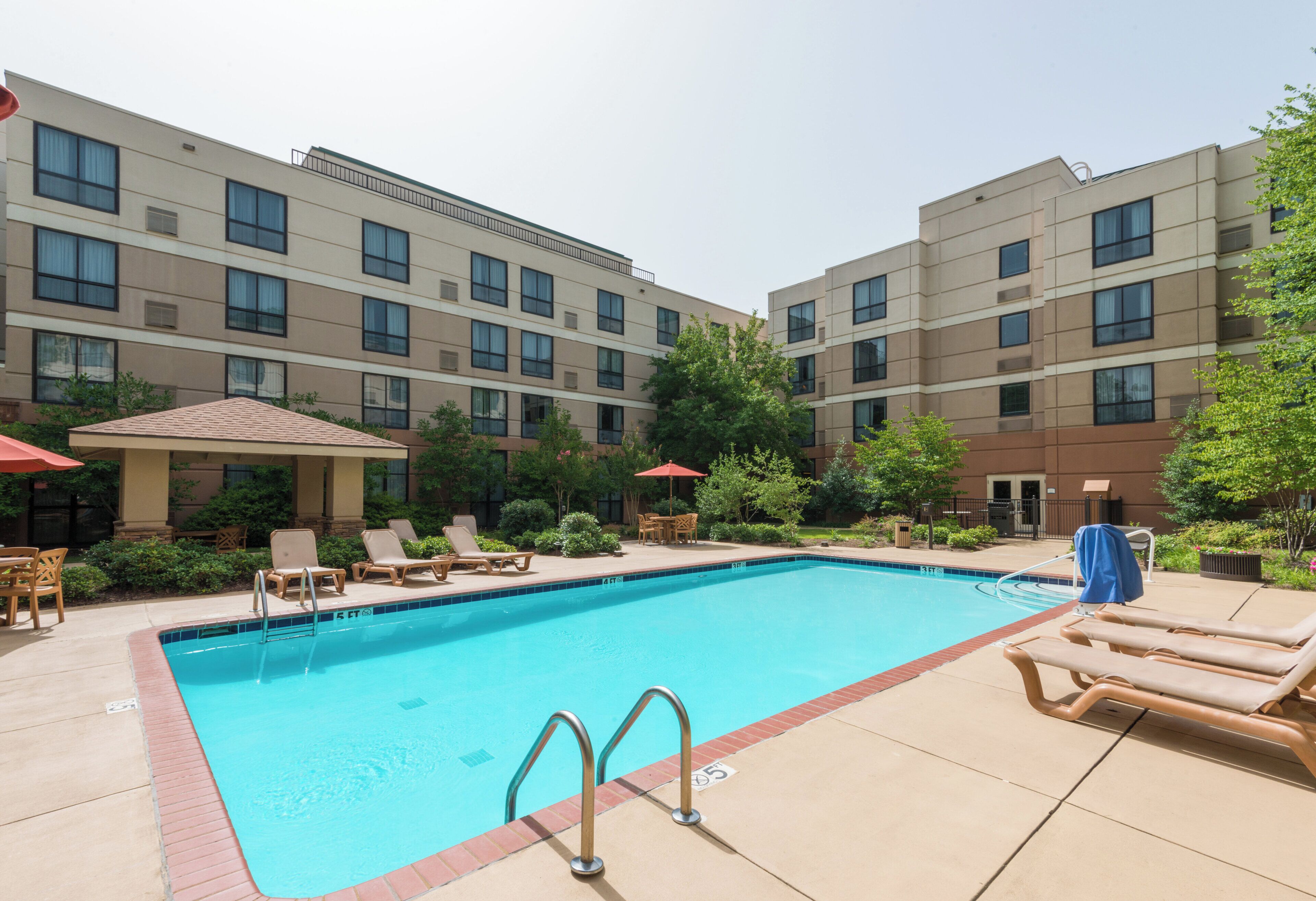 A swimming pool with lounge chairs and umbrellas, surrounded by a building with multiple windows and balconies.