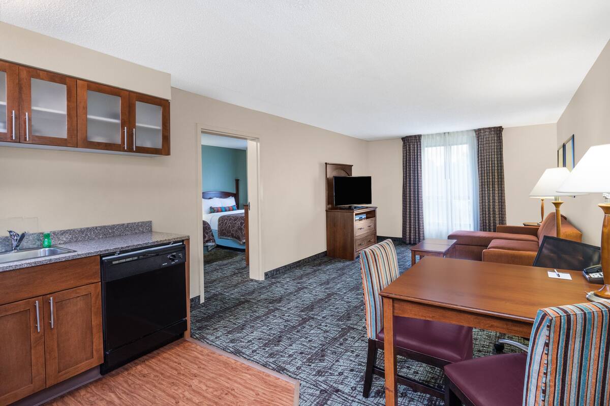 Habitación de hotel con kitchenette, comedor, televisor y cama.