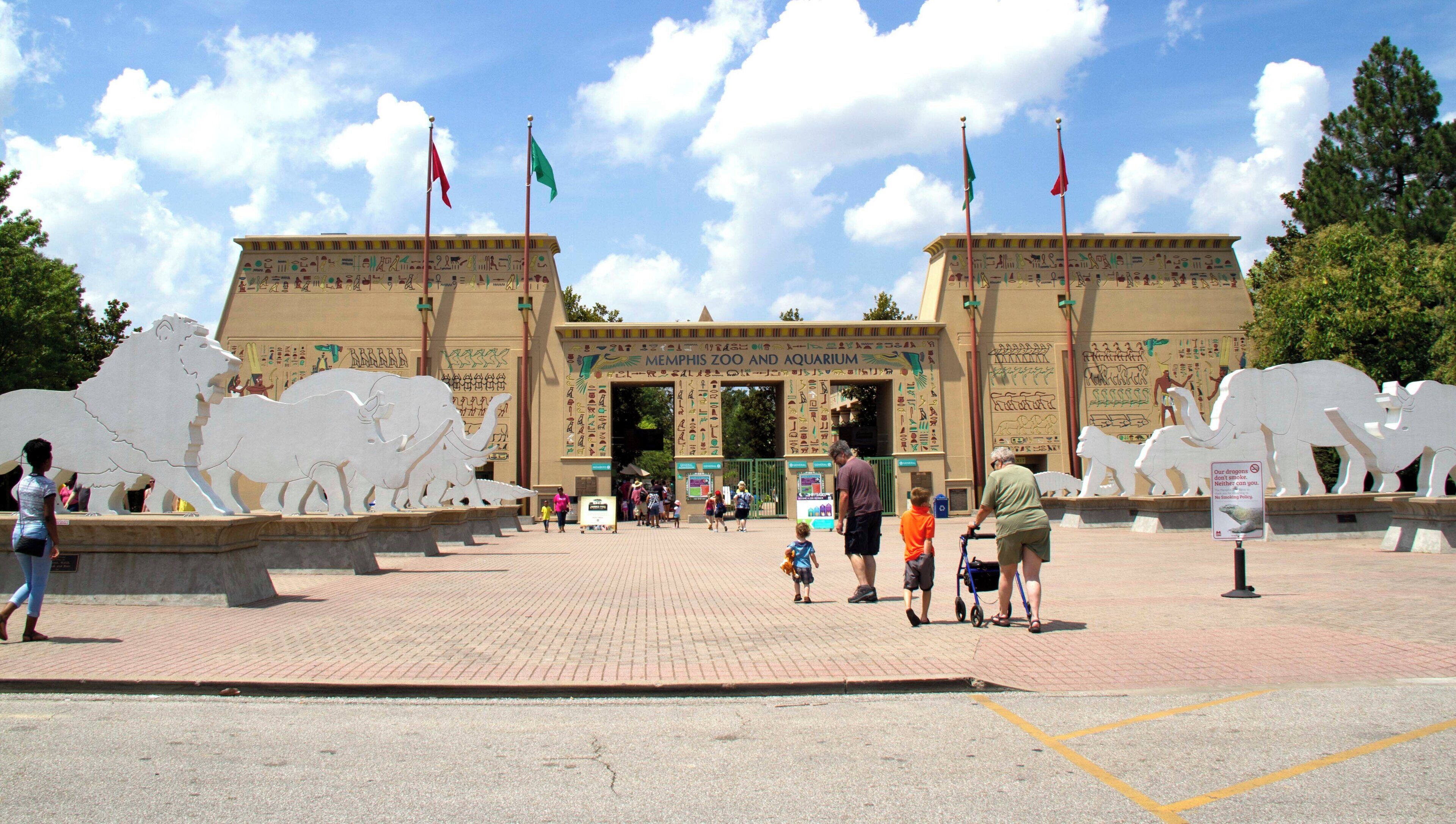 The entrance to a zoo with large animal sculptures and hieroglyphic decorations.