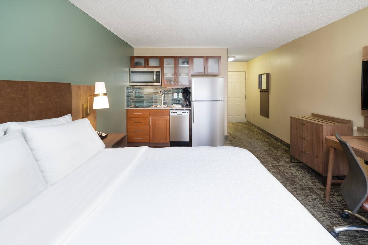 Una habitación de hotel con cama, escritorio, silla, microondas, refrigerador y una pequeña cocina.
