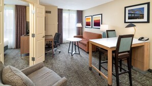 A hotel room with a bed, a desk, a chair, a sofa, a small table, and a lamp.