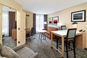 Habitación de hotel con cama, escritorio, silla, sofá, mesita y lámpara.