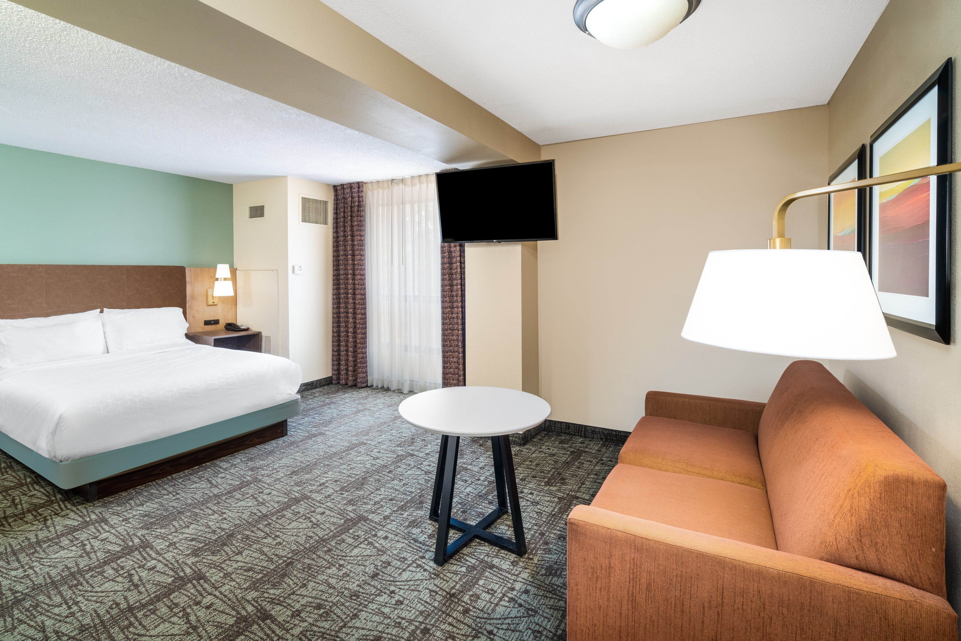 Una habitación de hotel con una cama, una mesita, un sofá, un televisor y una lámpara.