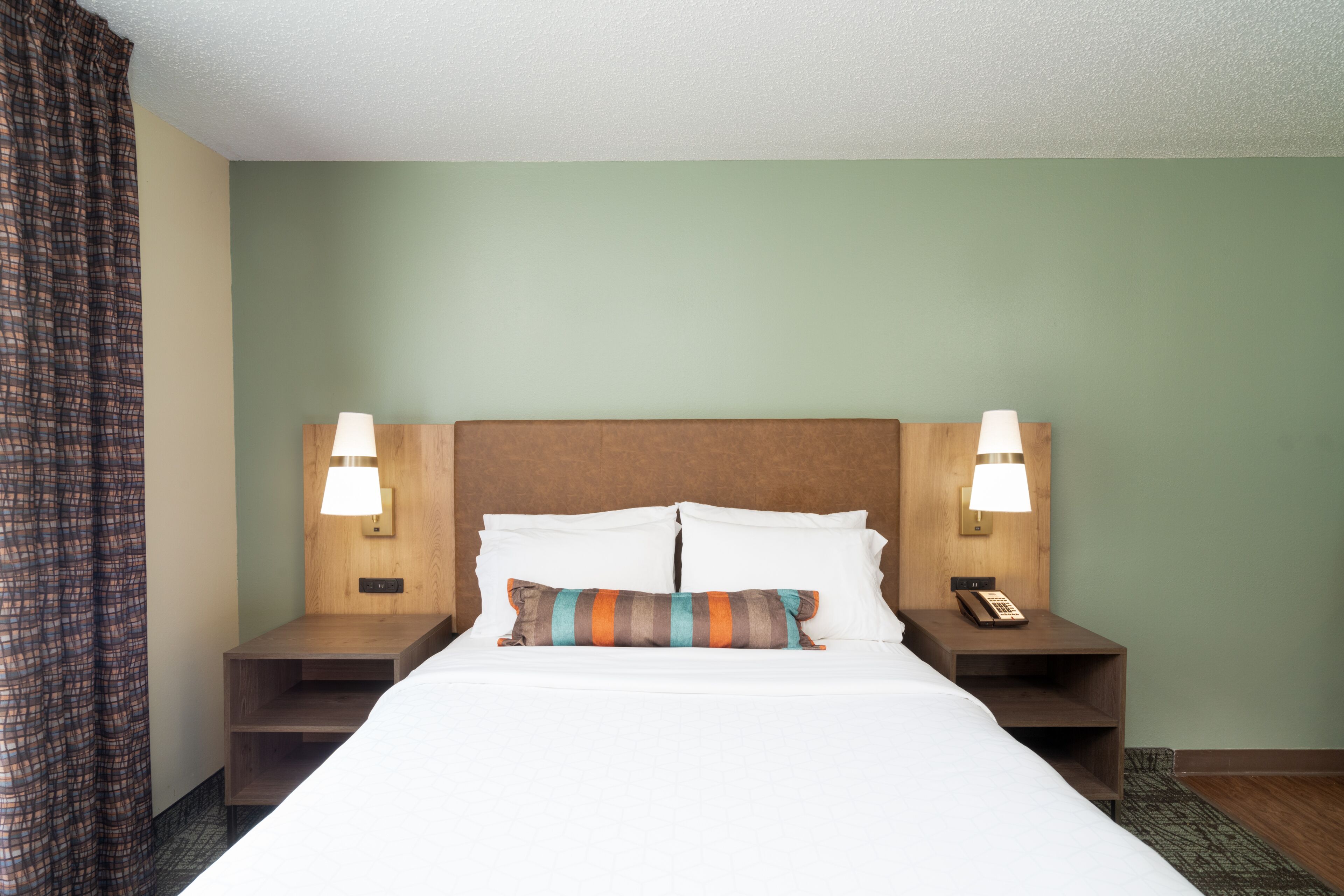 A hotel room with a large bed, two bedside tables with lamps, a telephone, and a striped pillow.