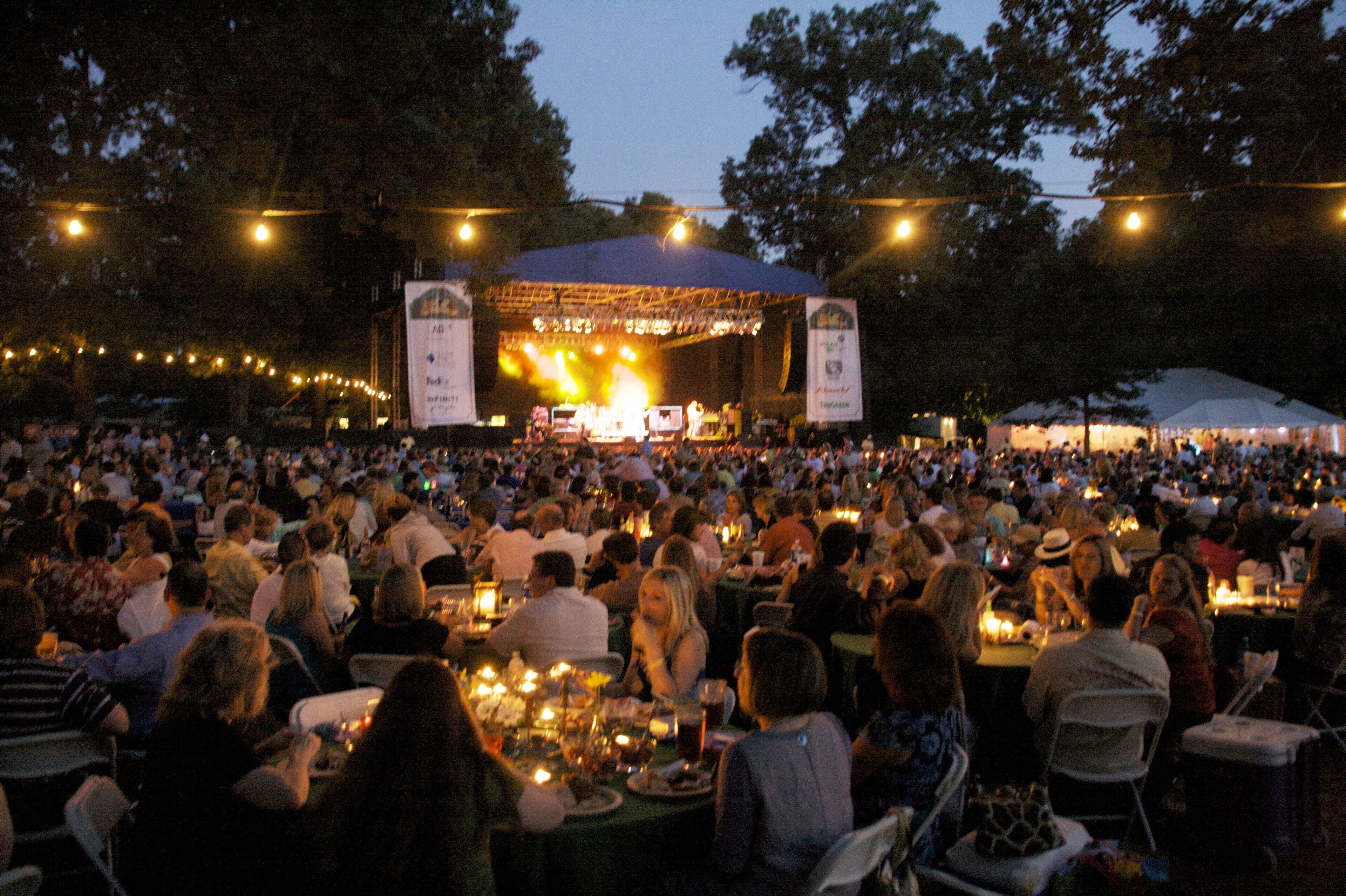 An outdoor event with a stage and audience seated at tables.