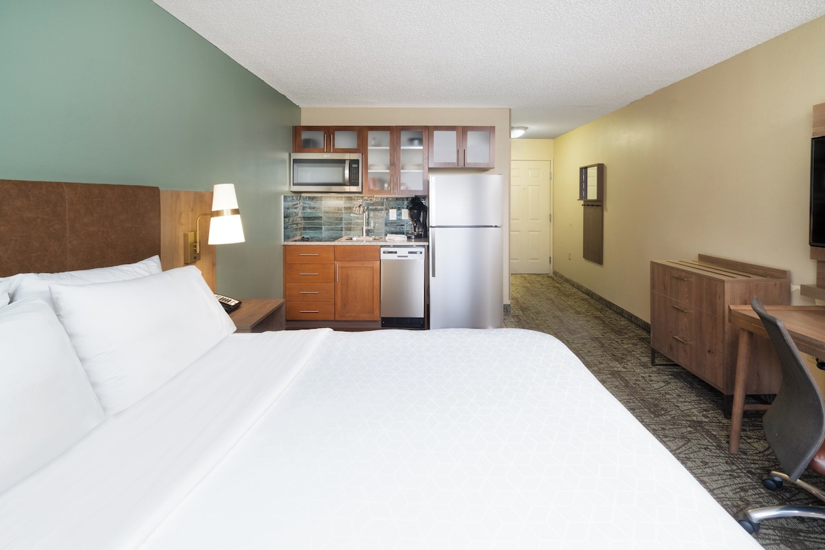 Una habitación de hotel con cama, escritorio, kitchenette y televisión.