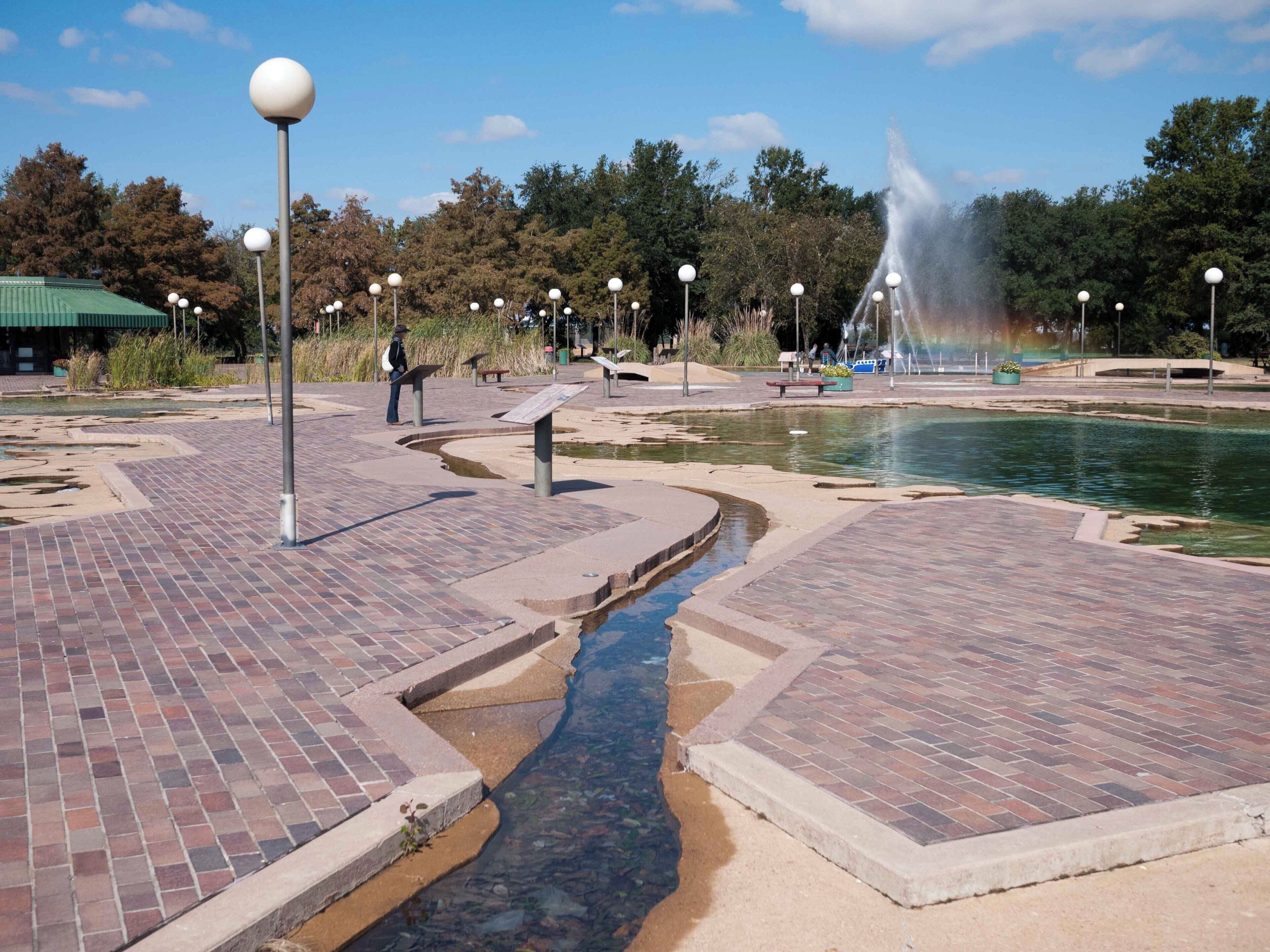 A park with a fountain, brick pathways, and informational signs.