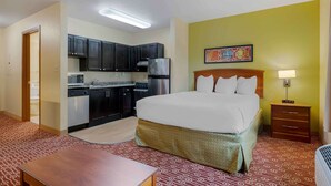Una habitación de hotel con una cama, un escritorio pequeño, un rincón americano y una mesita de noche con lámpara.
