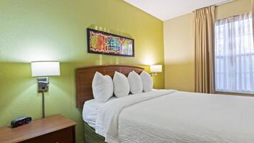 A hotel room with a bed, bedside lamps, a nightstand, a clock, and a painting on the wall.