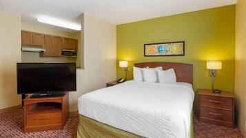 A hotel room with a bed, bedside lamps, a TV on a wooden stand, a small drawer, a microwave, and a painting on the wall.