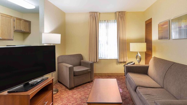 Habitación de hotel con una televisión de pantalla plana, dos sofás, una mesita de centro, una lámpara y una ventana con cortinas.