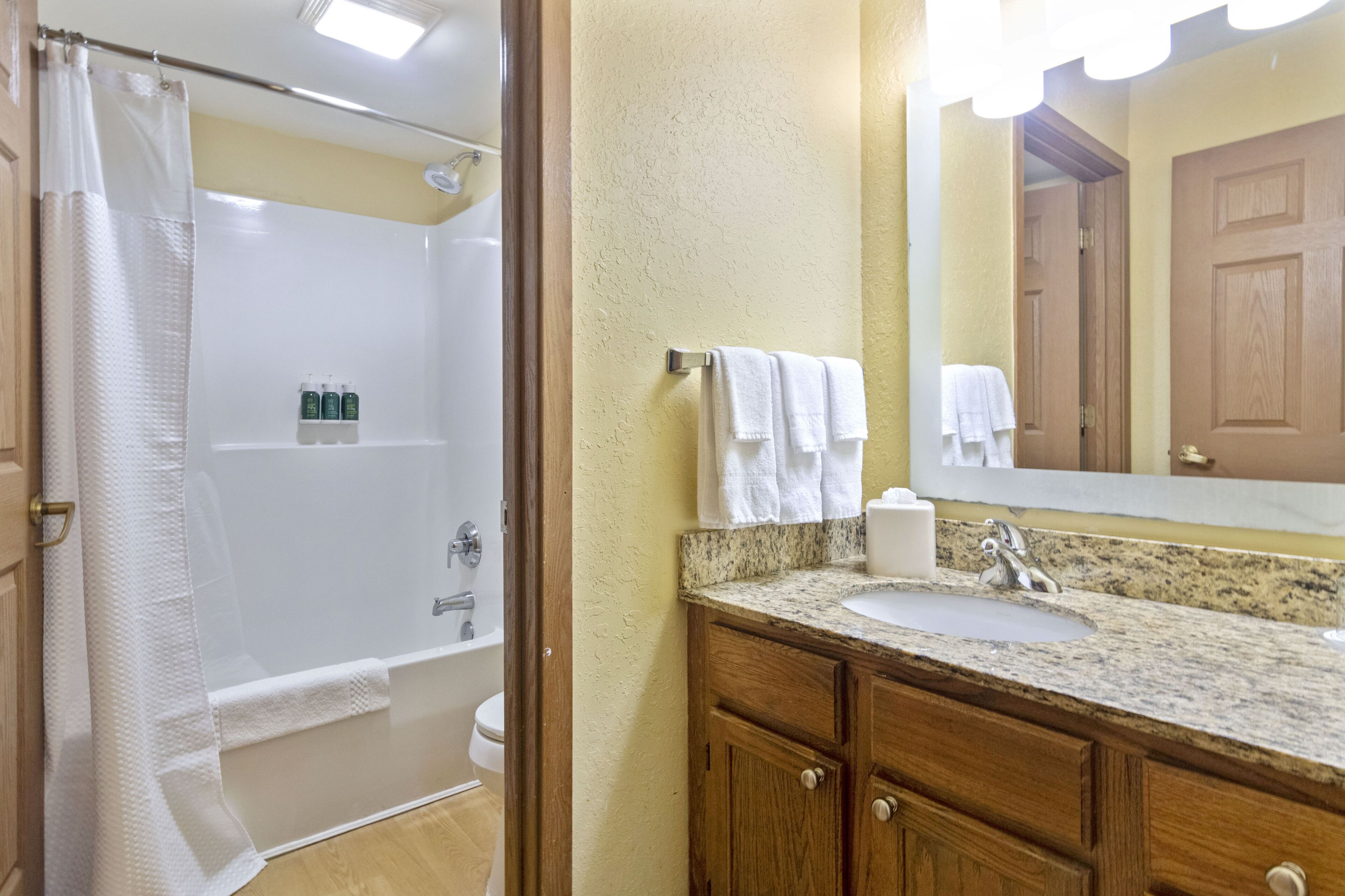 A bathroom with a shower, toilet, sink, and wooden vanity.