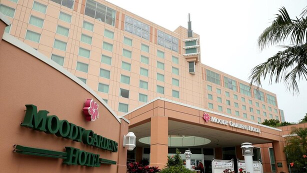 The exterior of the Moody Gardens Hotel with a large entrance, a signboard, and a well-maintained garden area.