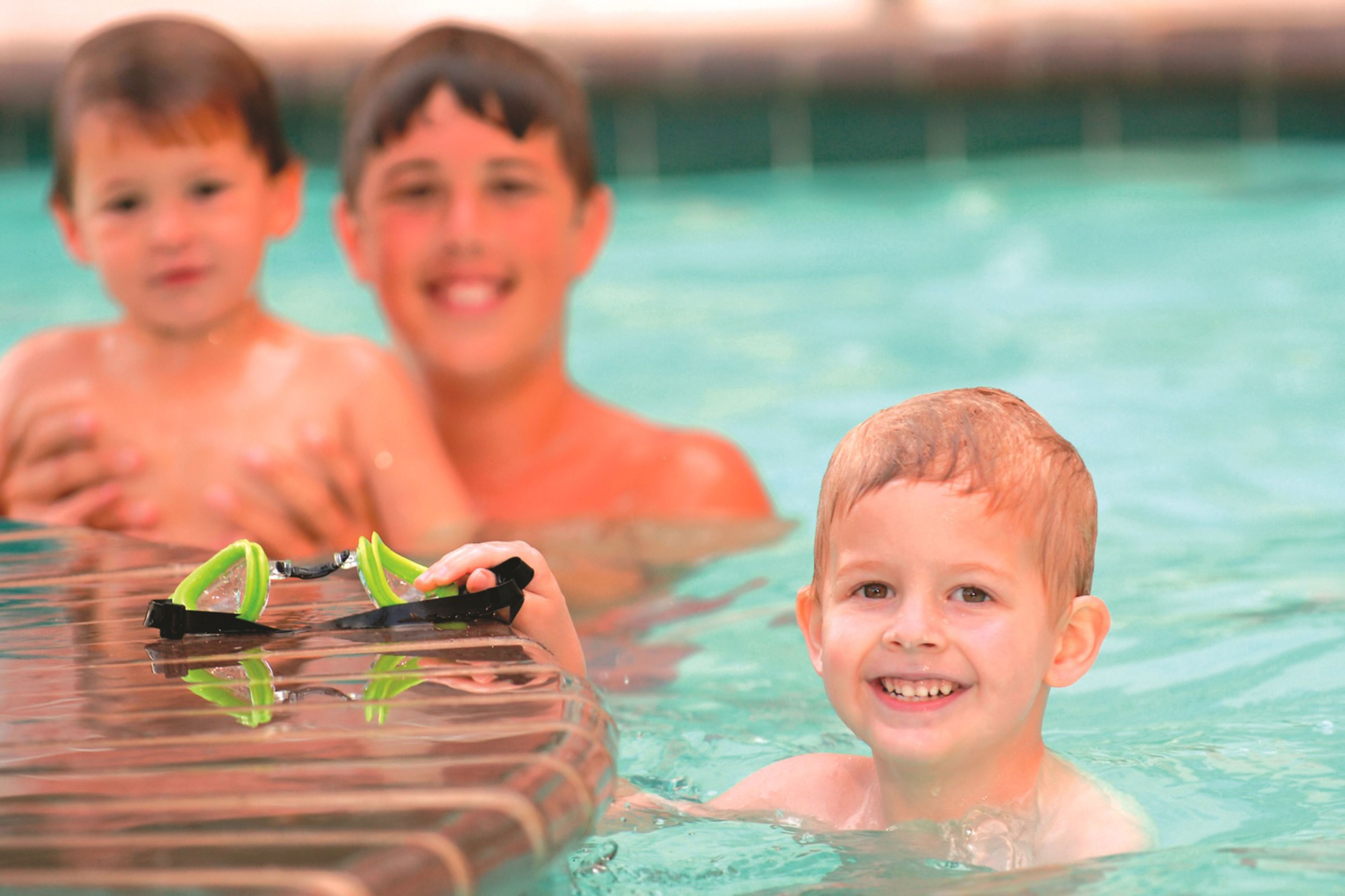 A pool with clear water, a floating platform, and a child holding goggles.