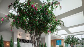 A restaurant with round tables, wooden chairs, and a central tree with pink flowers.
