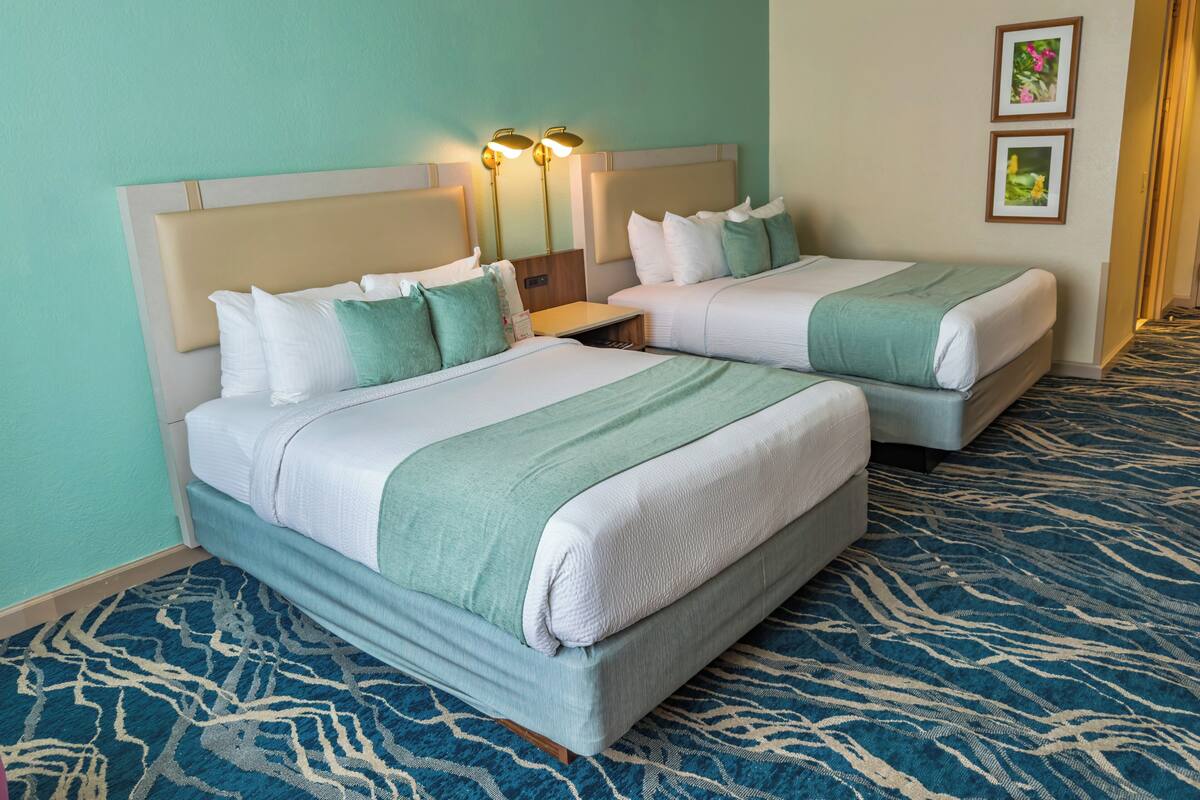 Une chambre d’hôtel avec deux lits, une table de chevet et une lampe fixée au mur.