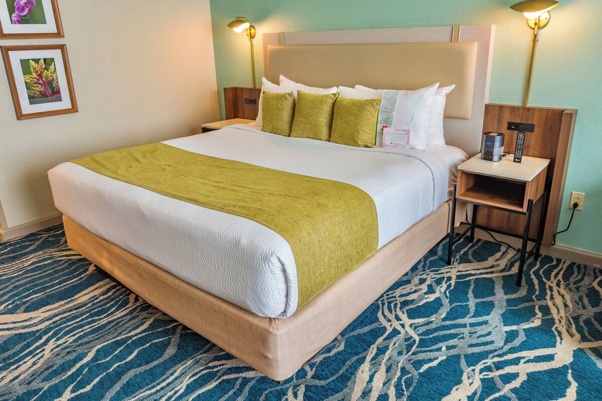 Une chambre d’hôtel avec un grand lit, deux tables de chevet, une petite table, une lampe et un téléviseur fixé au mur.
