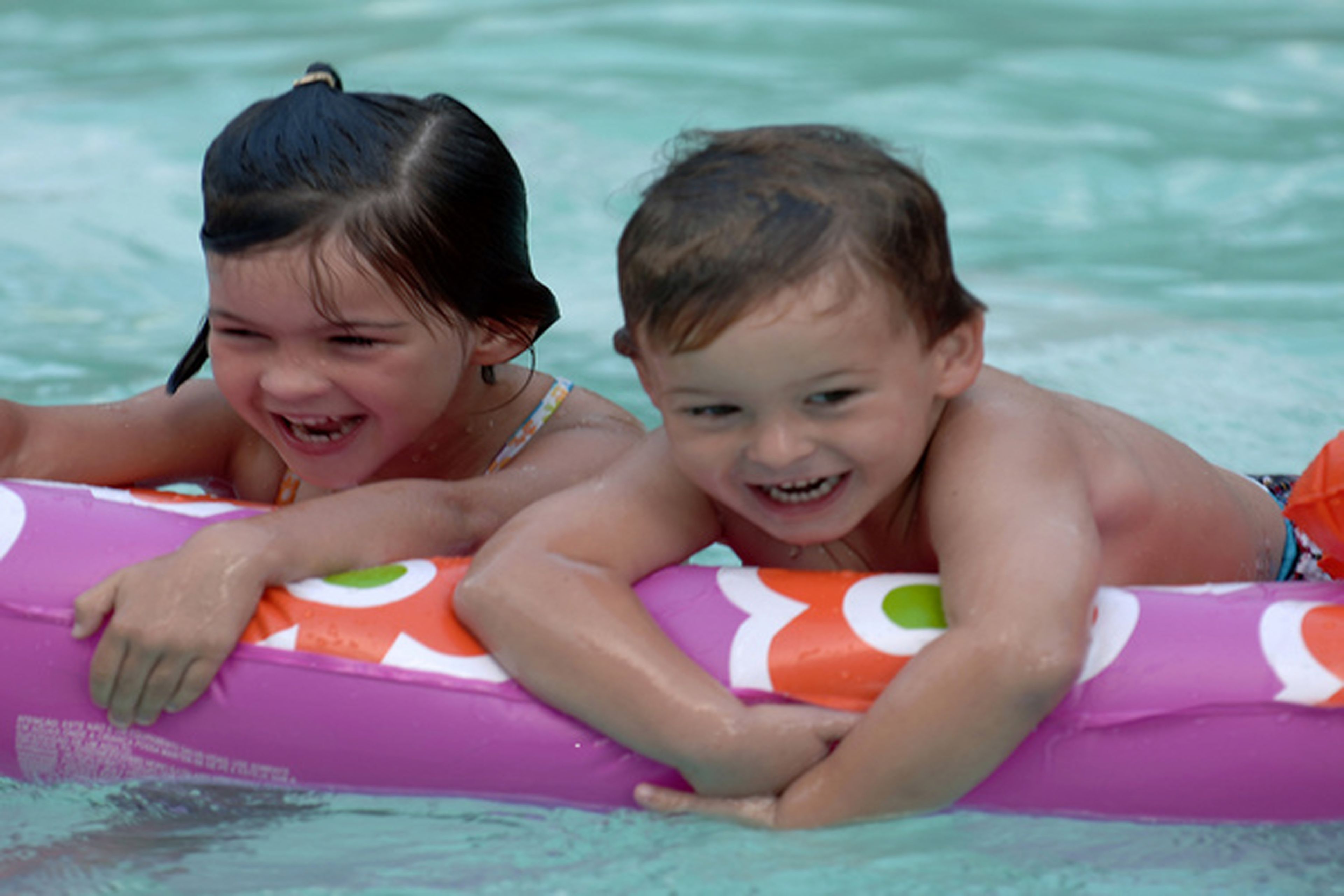 Two children lying on a colorful inflatable float in a swimming pool.