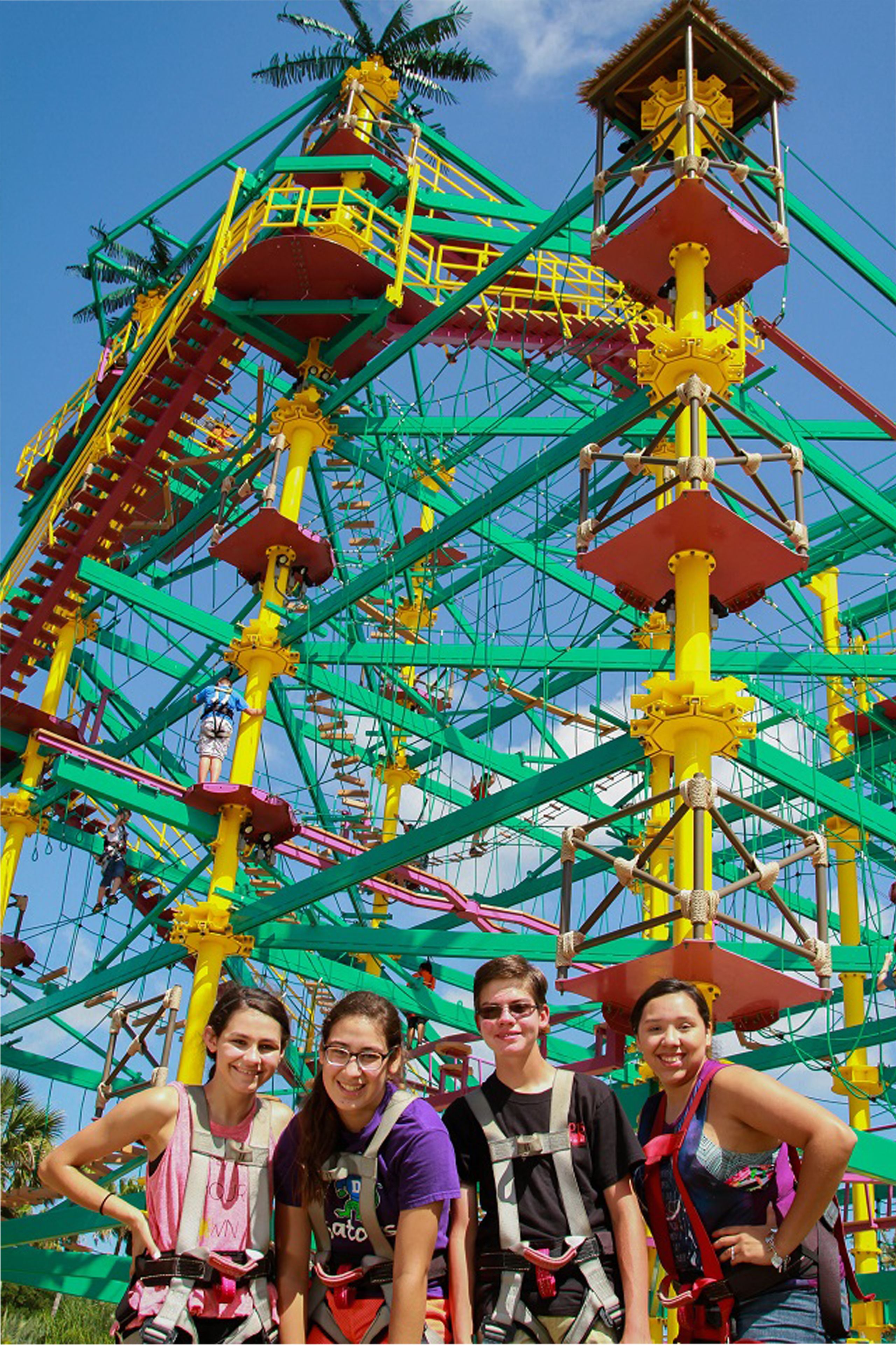 A group of people standing in front of a large, colorful amusement park ride with a tall structure and multiple levels.