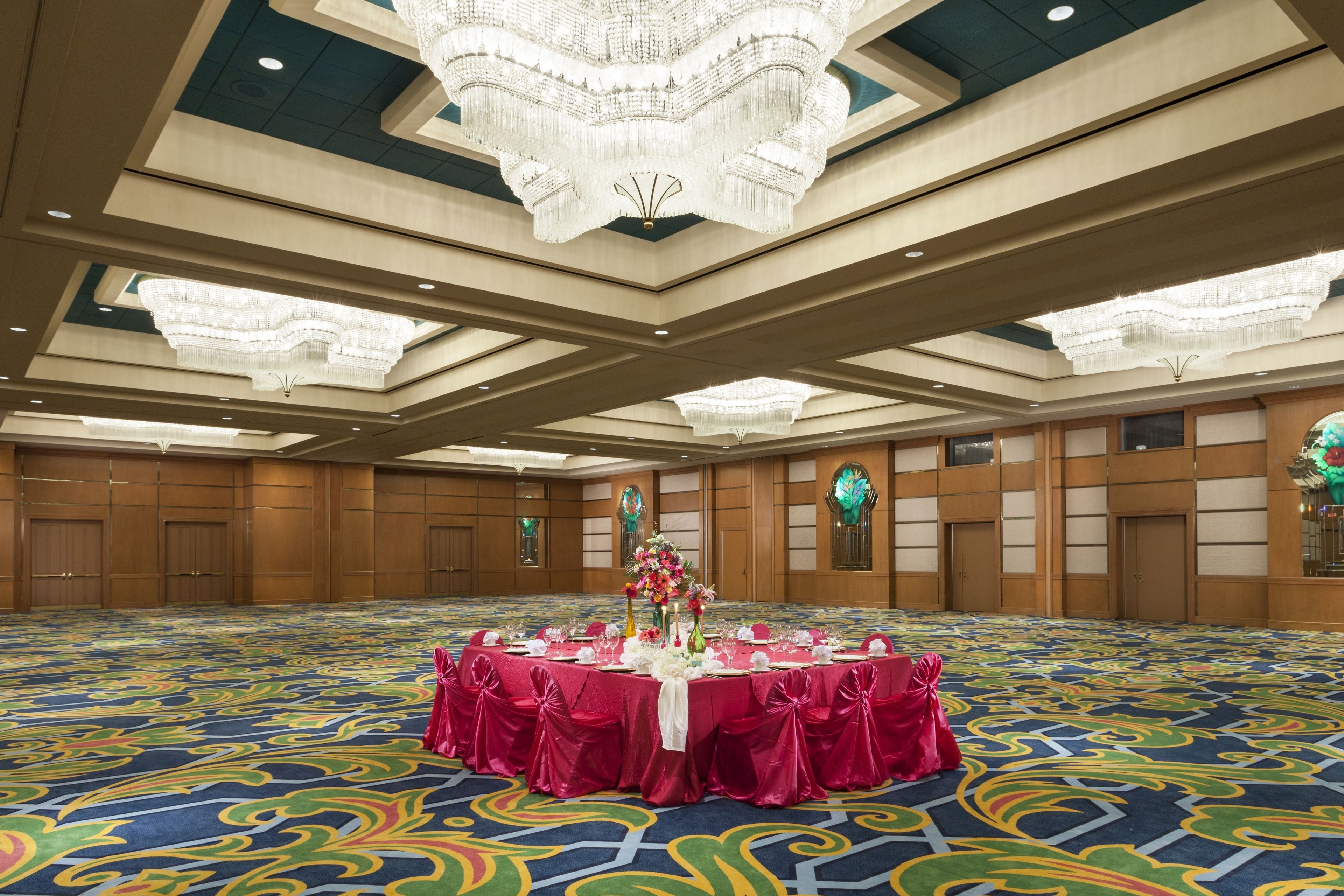 A banquet hall with a large round table set for a formal event, featuring a floral centerpiece and red tablecloths.
