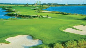Un campo de golf con una masa de agua, bunkers de arena y un edificio a lo lejos.