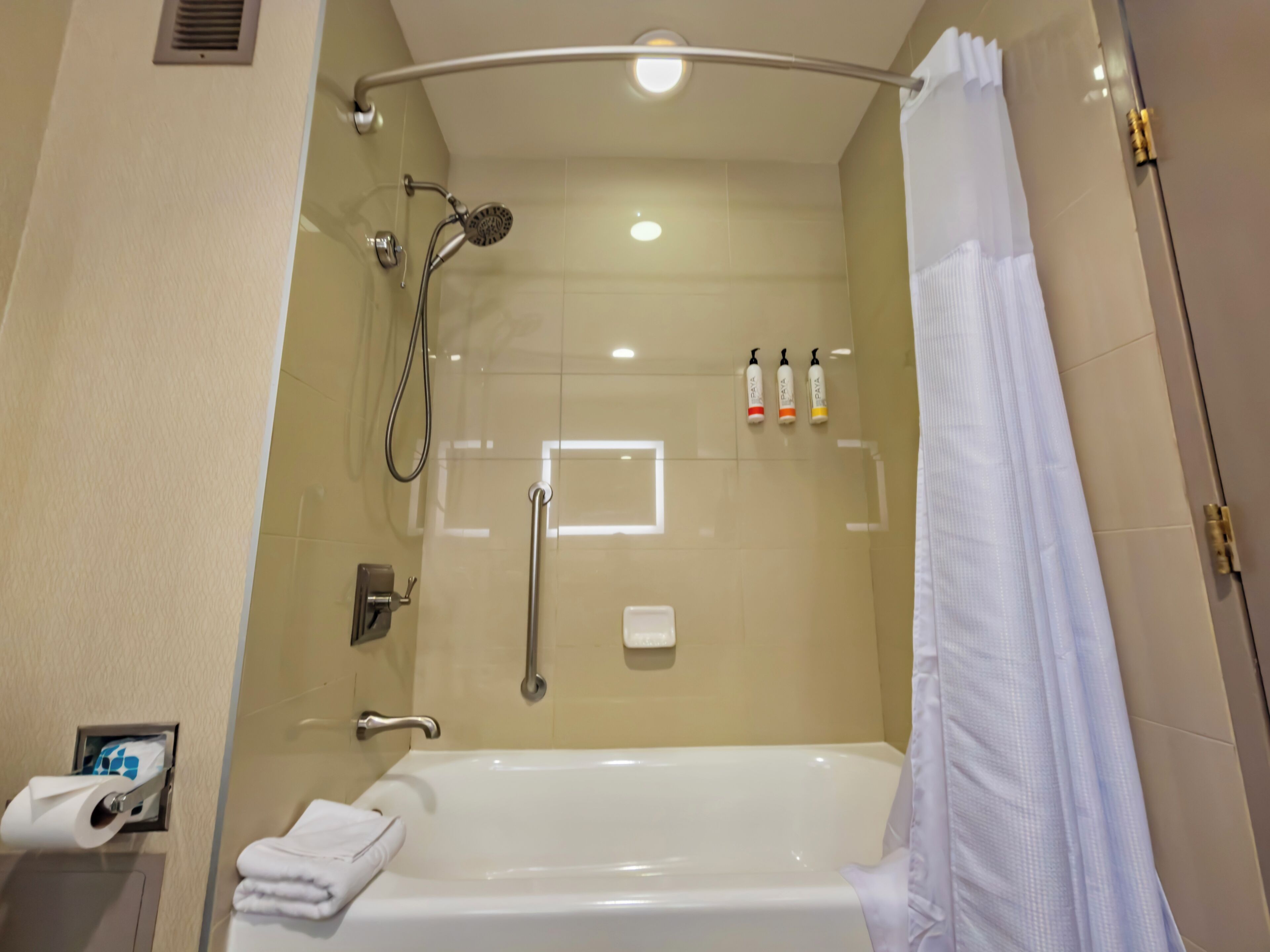 Un baño moderno con ducha de vidrio, una bañera blanca, un perchero para toallas y un secador de manos.