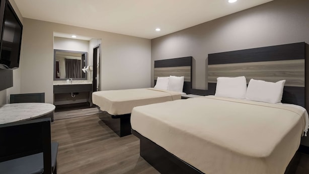 A hotel room with two beds, a TV, a desk, and a mirror. - Rodeway Inn San Bernardino - Colton (San Bernardino)