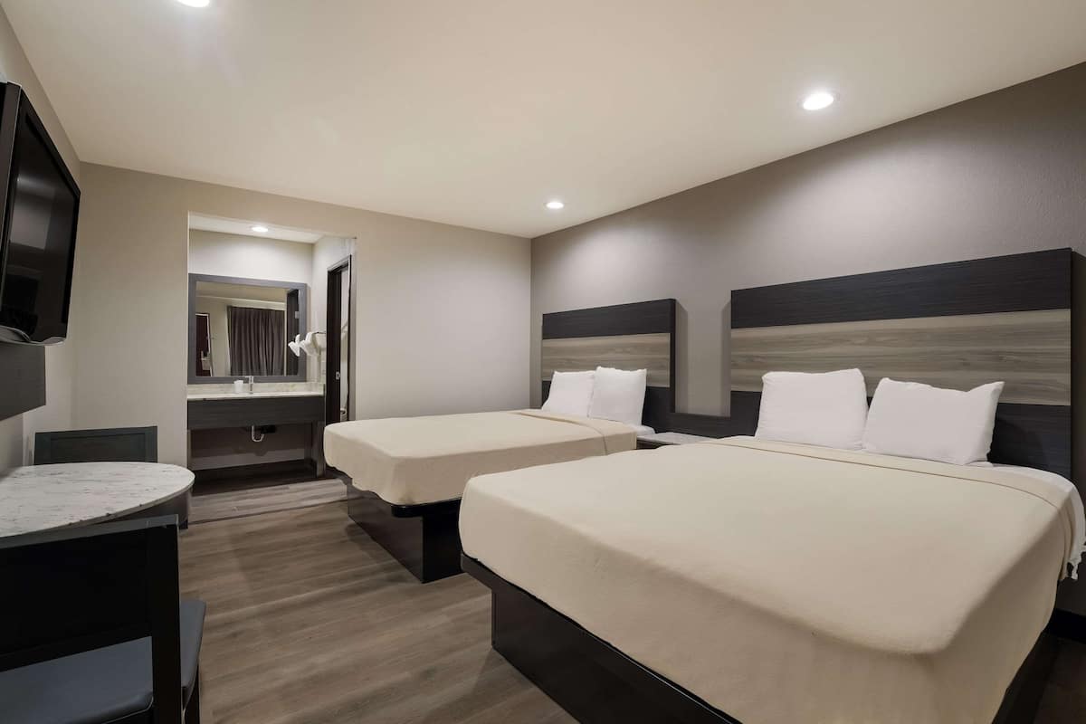 A hotel room with two beds, a TV, a desk, and a mirror.