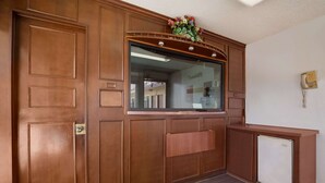 A wooden reception desk with a glass window, a telephone, and a small refrigerator. - Rodeway Inn San Bernardino - Colton (San Bernardino)