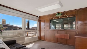 A modern living room with a leather sofa, a wooden cabinet, and a large window offering a city view. - Rodeway Inn San Bernardino - Colton (San Bernardino)