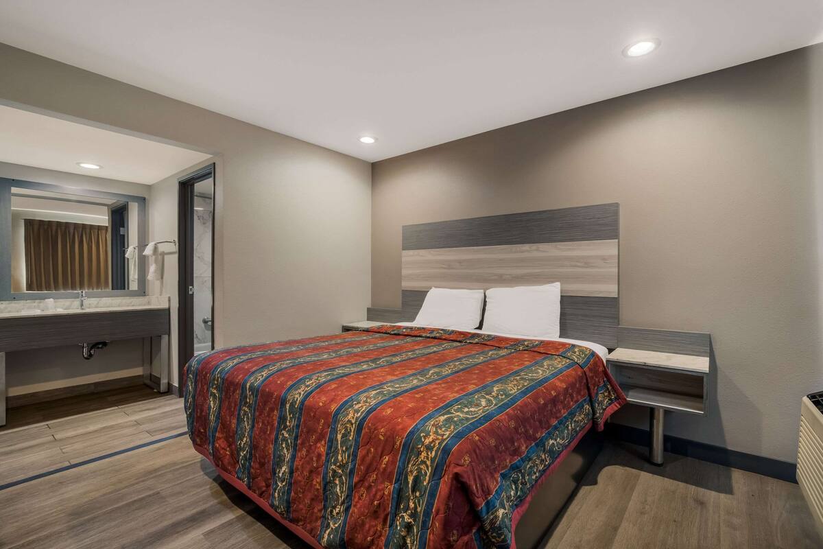 A modern bedroom with a large bed, a nightstand, a mirror, and a built-in shelf.