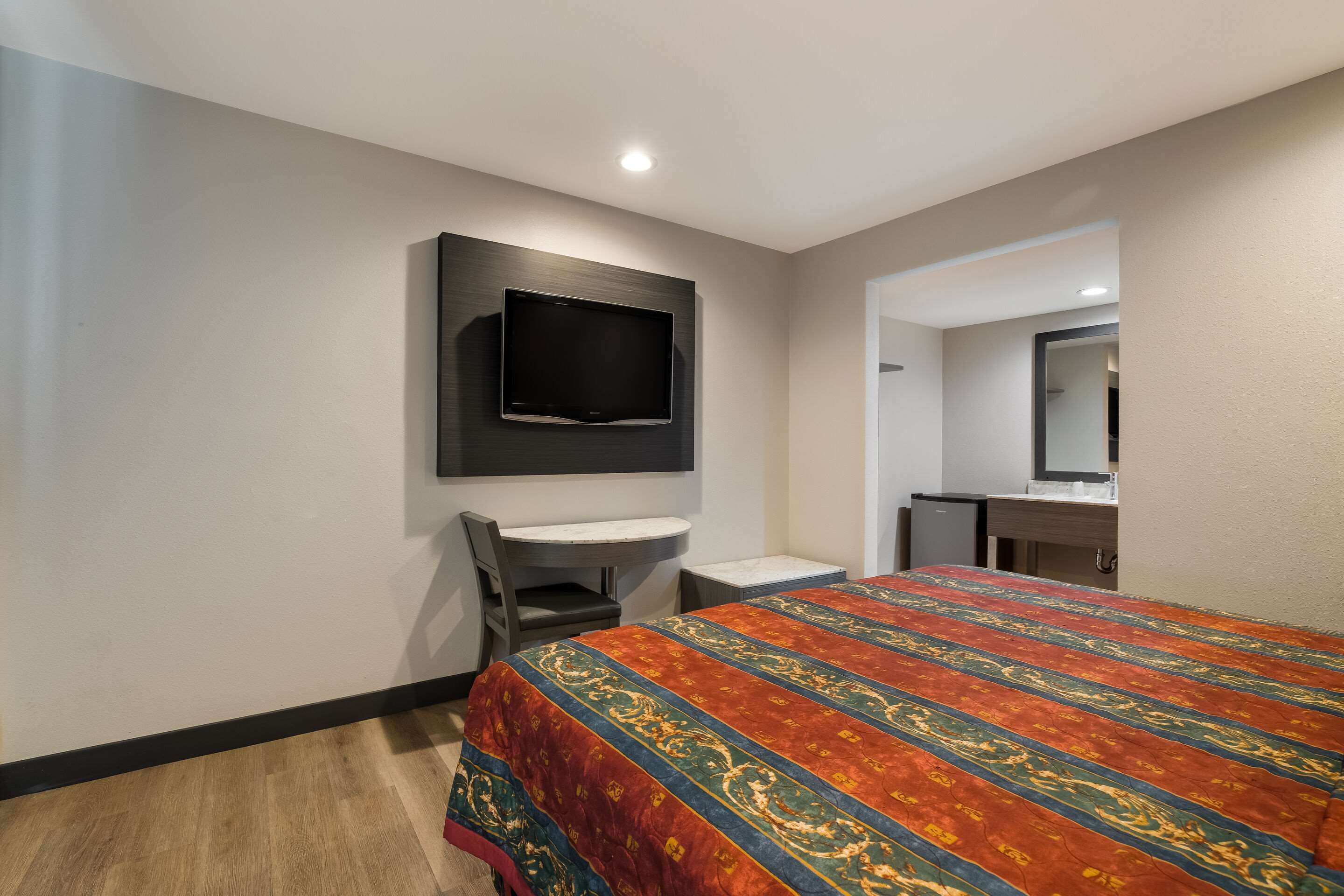 Une chambre d’hôtel équipée d’un lit, d’un bureau, d’une chaise, d’un téléviseur fixé au mur et d’une petite kitchenette.