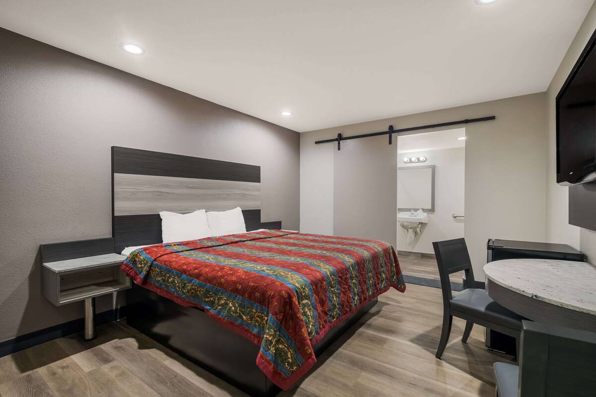 A modern hotel room with a bed, bedside table, chair, and a round dining table.