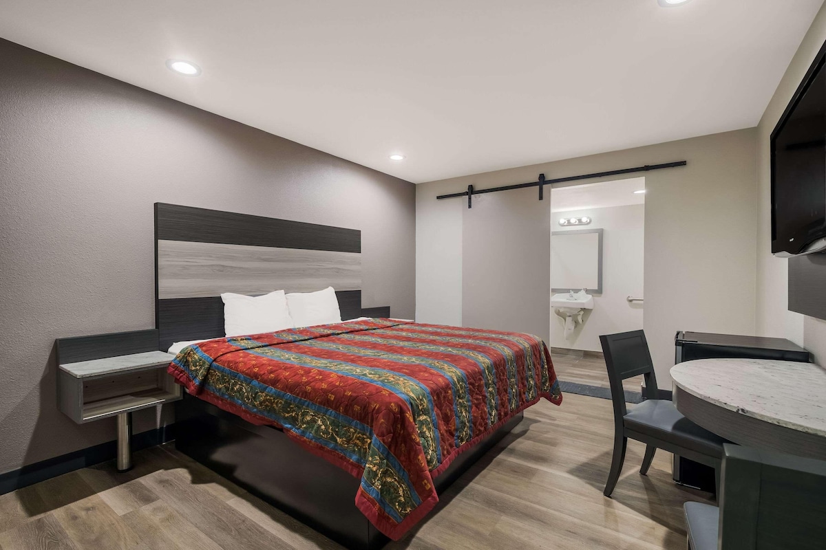 A modern hotel room with a bed, bedside table, chair, and a round dining table.