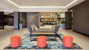 Eine moderne Lobby mit einer runden Sitzecke, drei orangefarbenen Hocker und einem gemusterten Teppich.