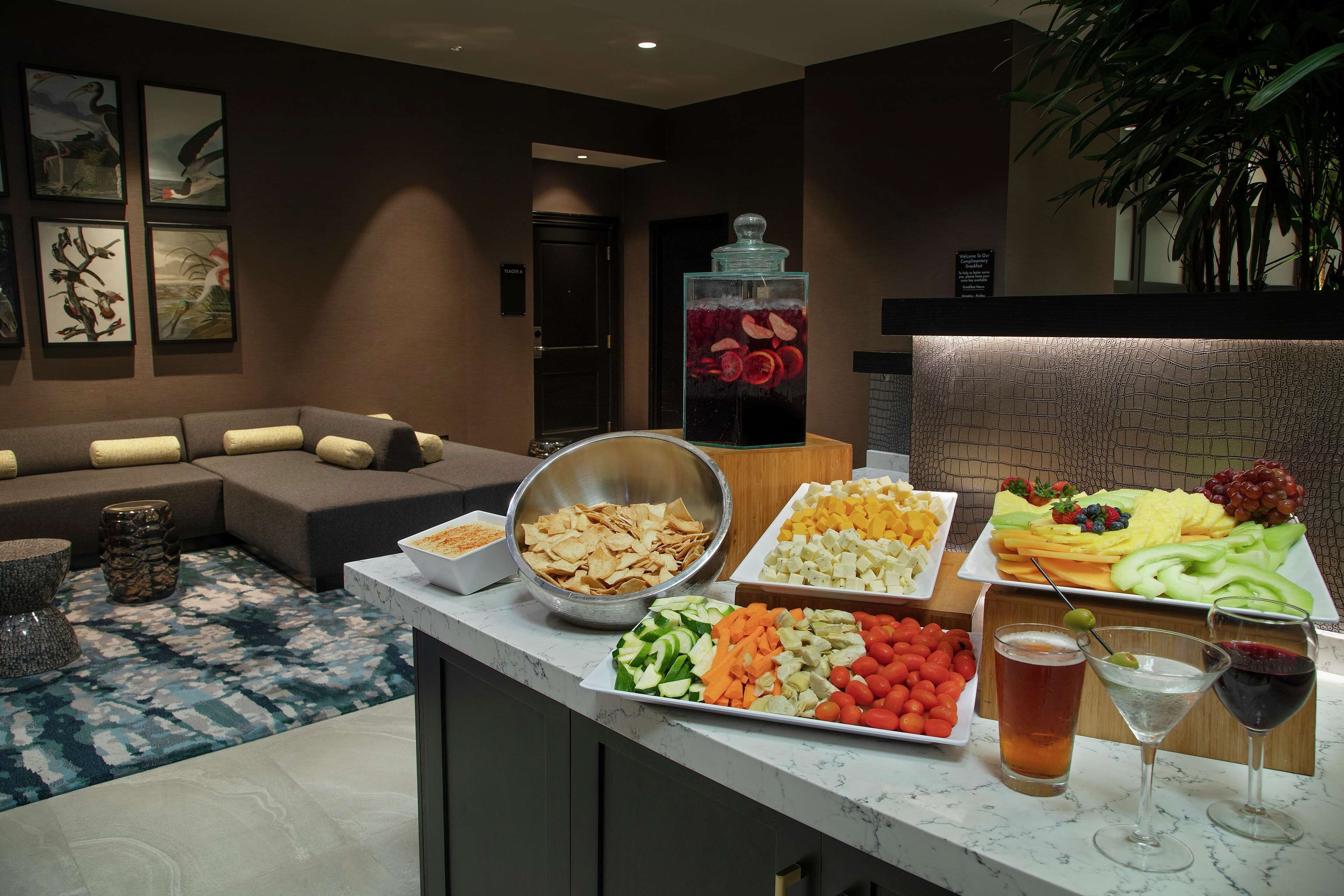 Uma área de estar bem equipada com sofá, mesa de buffet com diversos alimentos e espaço de bar com bebidas.
