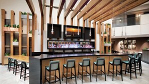 Eine moderne Bar mit einer langen Theke, mehreren Barhocker und einem Fernsehbild, das einen Sonnenuntergang zeigt.