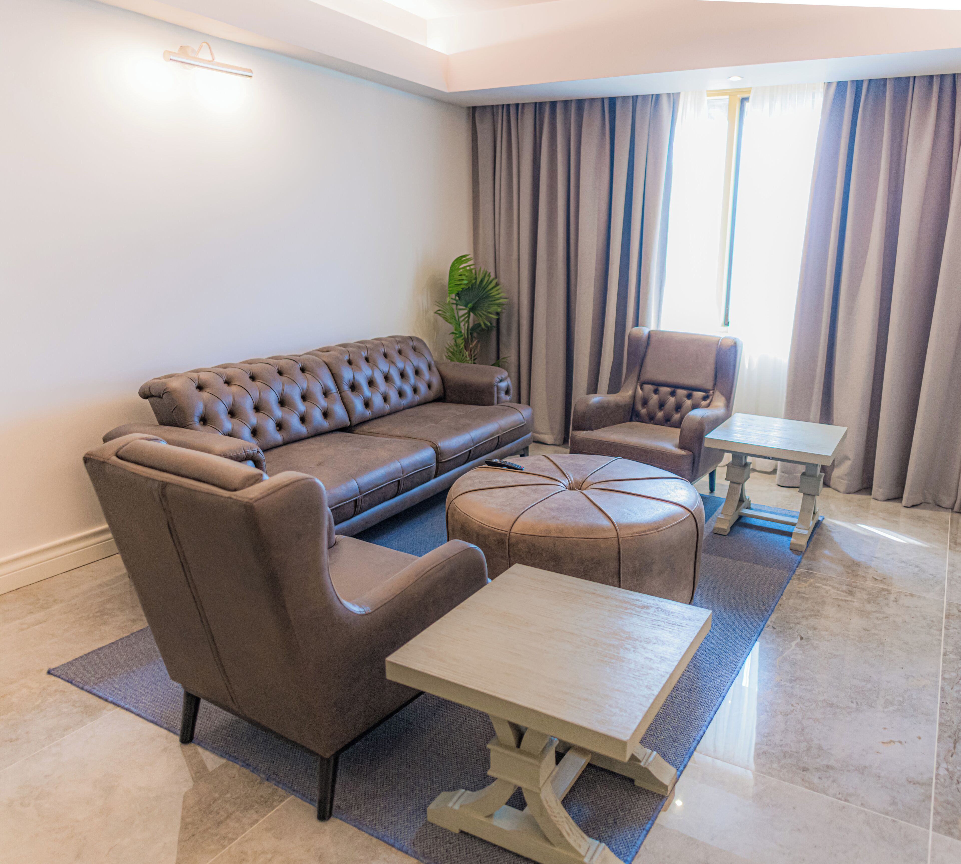 Una sala de estar moderna con un sofá de cuero marrón, un sillón a juego, una mesita de centro de madera y una mesita auxiliar.