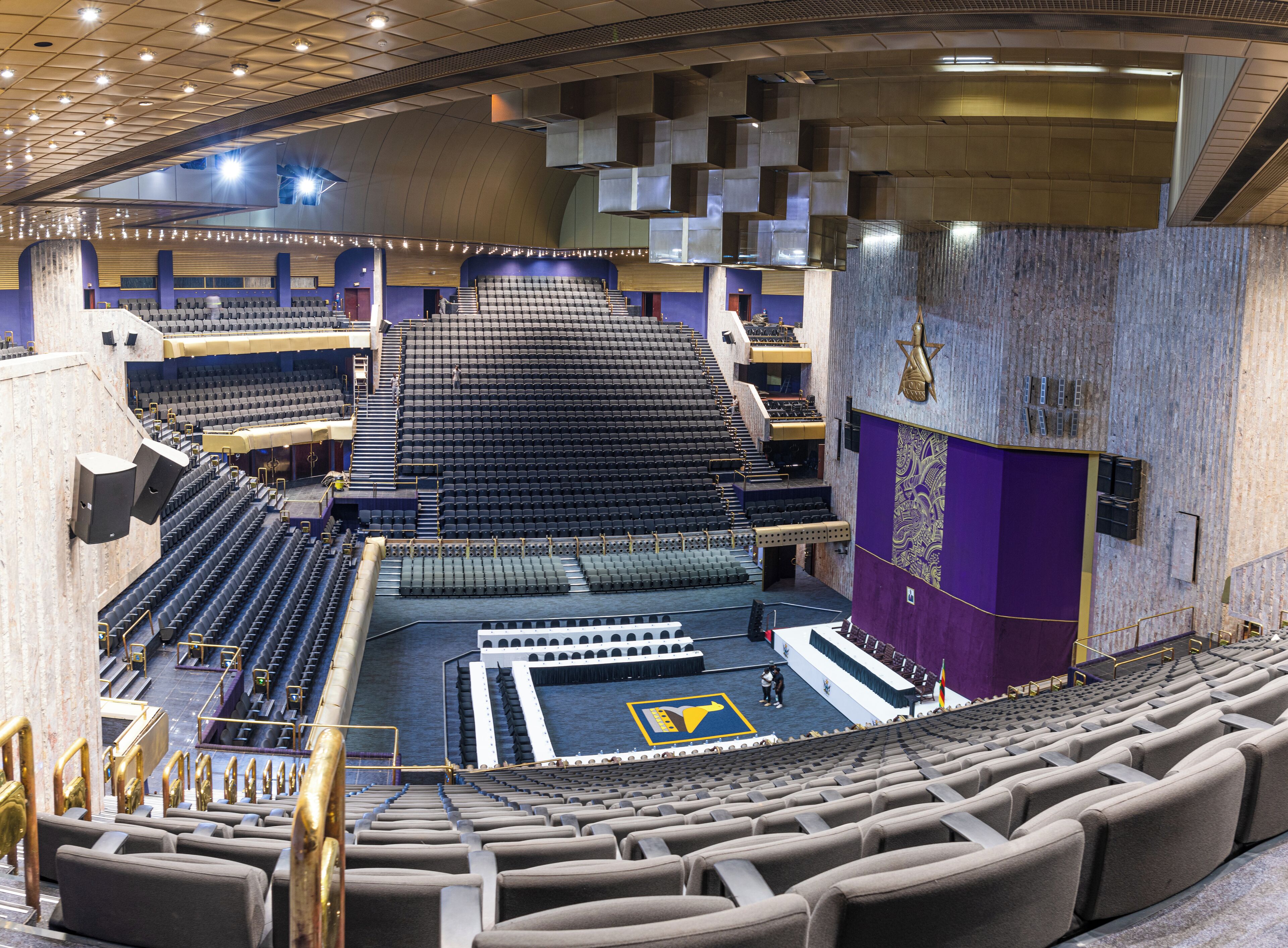 Un vaste auditorium intérieur doté de gradins, d’une scène et d’un grand symbole en forme d’étoile sur le mur.