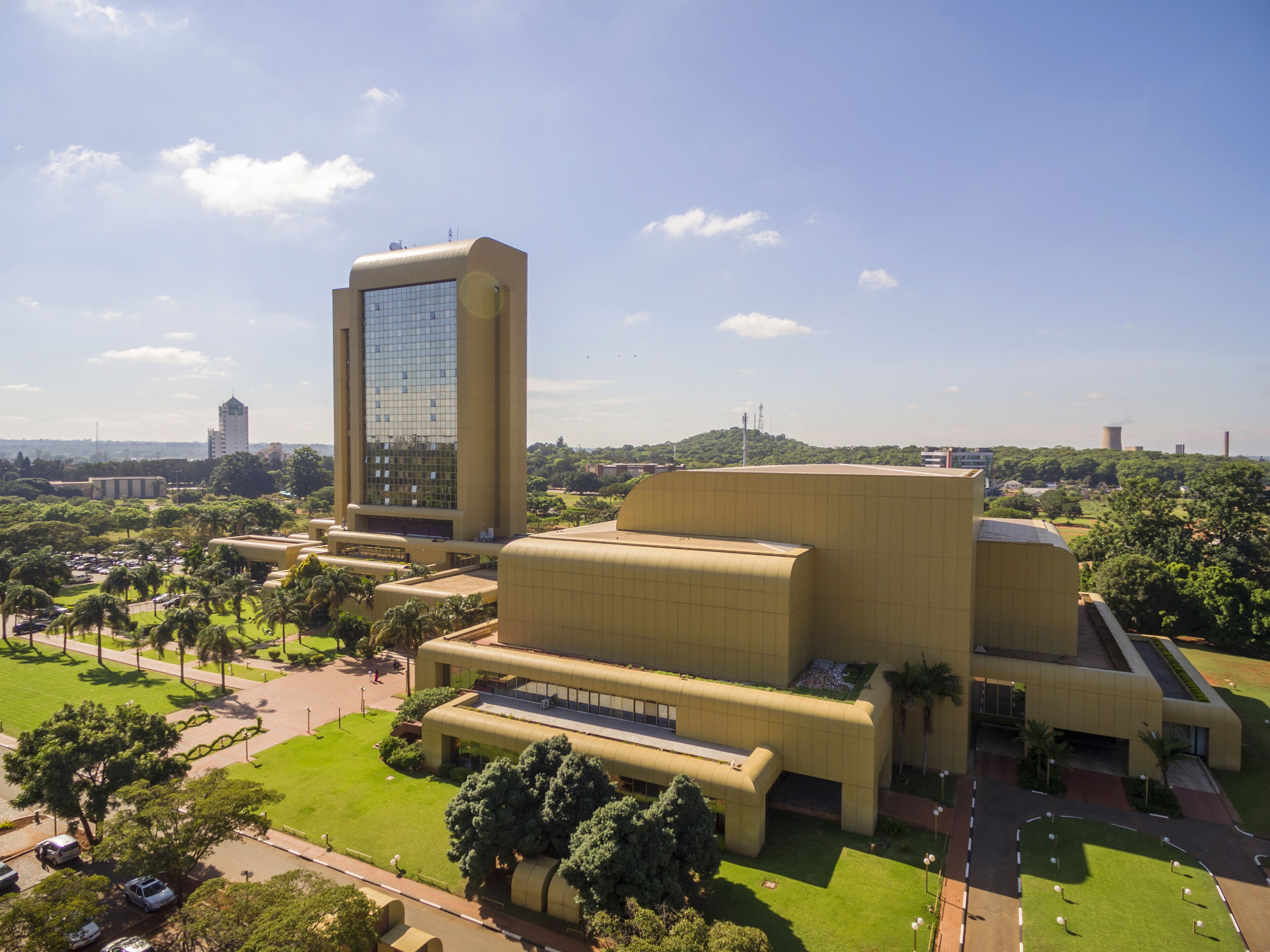 A large, modern building with a prominent glass tower and expansive green lawns.