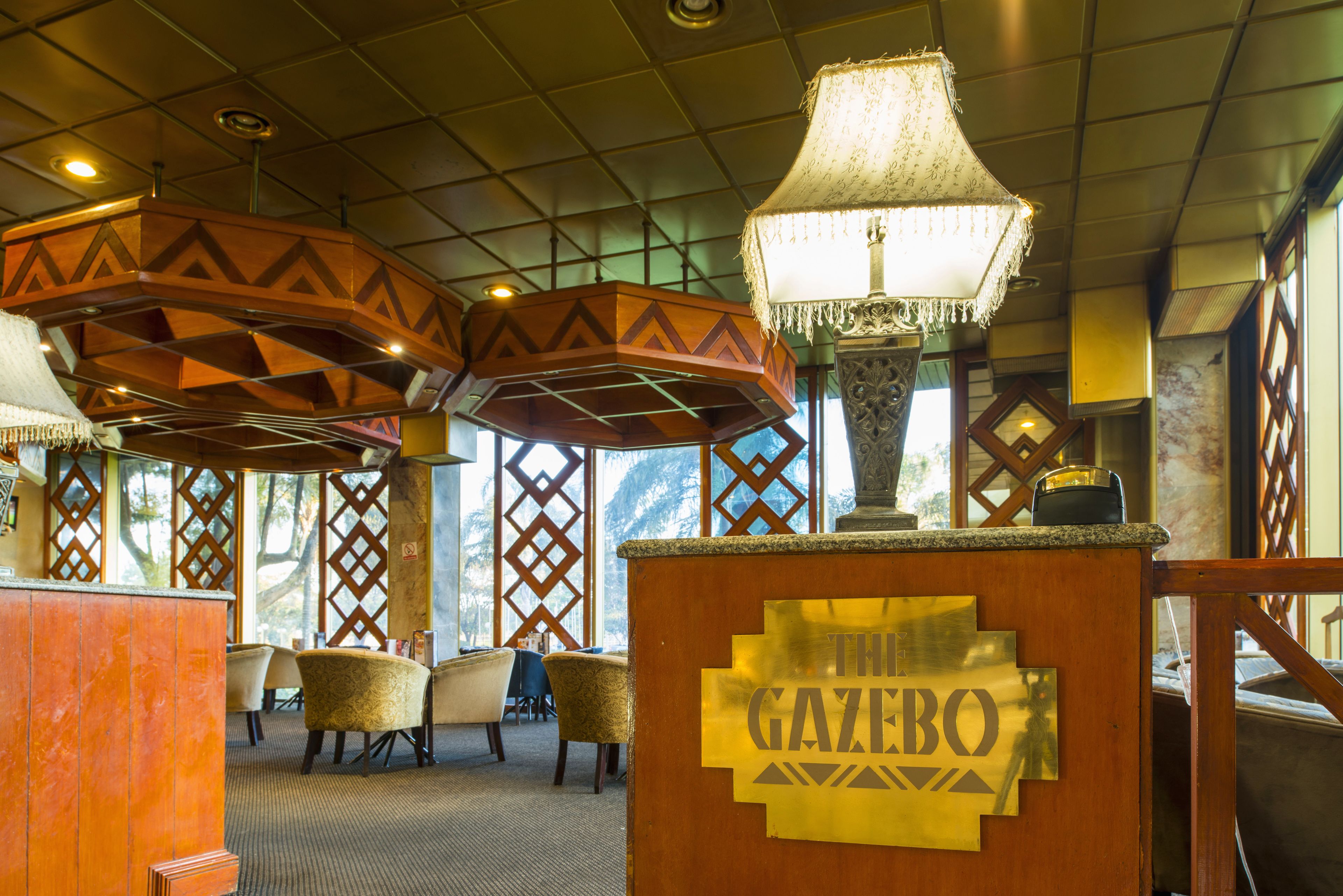 A lobby with a reception desk labeled "The Gazebo," featuring geometric wooden decor and a hanging lamp.