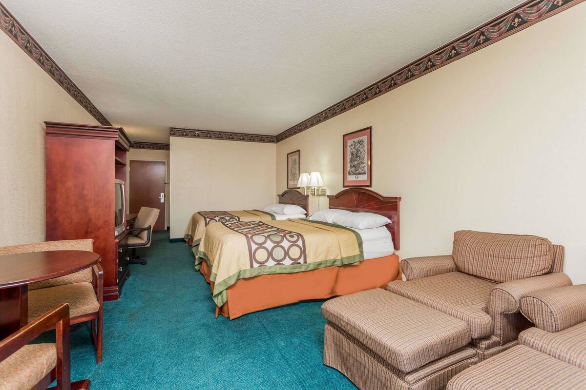 Quarto de hotel com uma cama, uma escrivaninha, uma cadeira, um sofá e piso coberto por carpete.