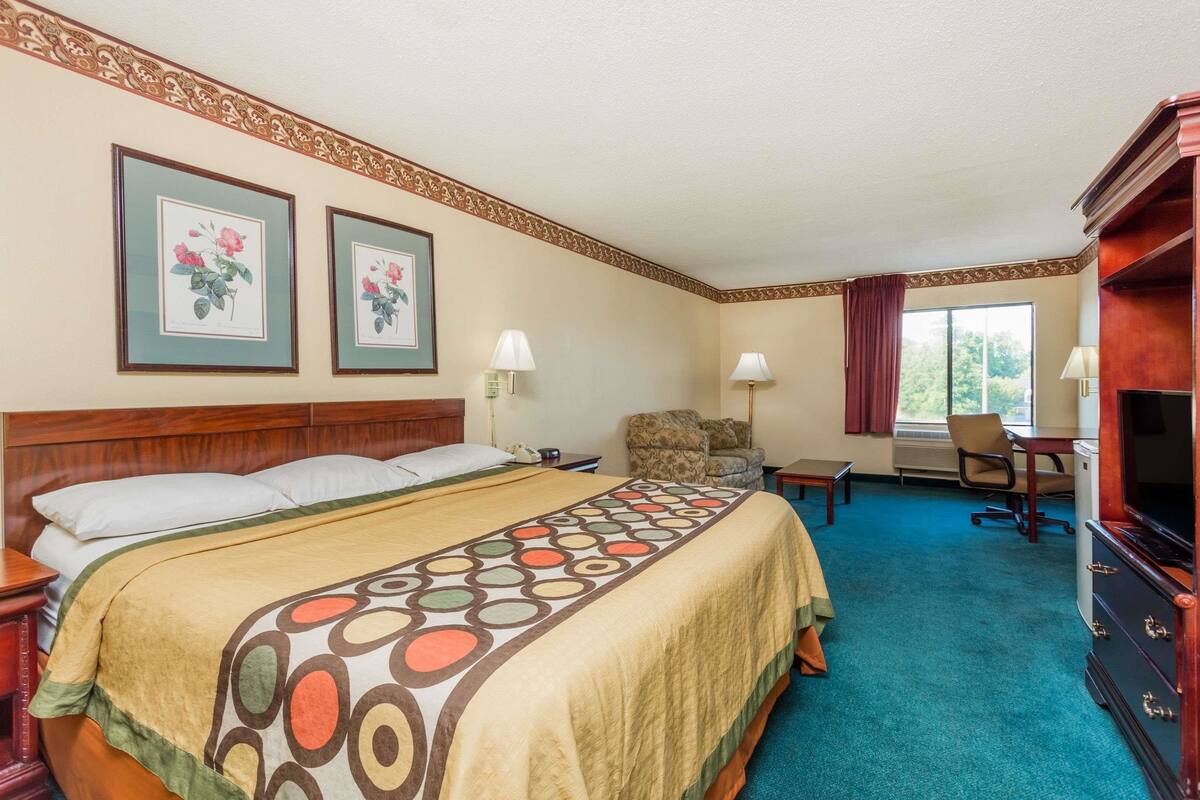 Quarto de hotel com uma cama grande, duas quadros com flores, uma escrivaninha, uma cadeira e uma televisão.