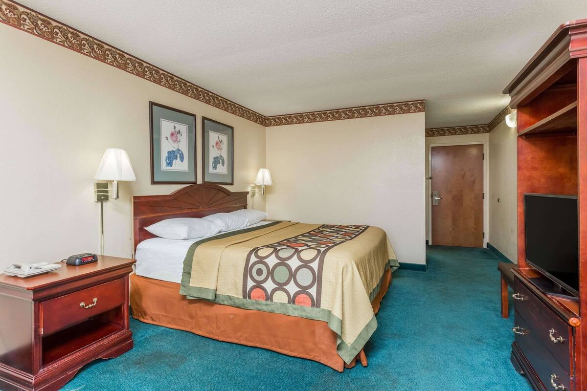 Quarto de hotel com cama, mesas de cabeceira, televisão e quadros nas paredes.