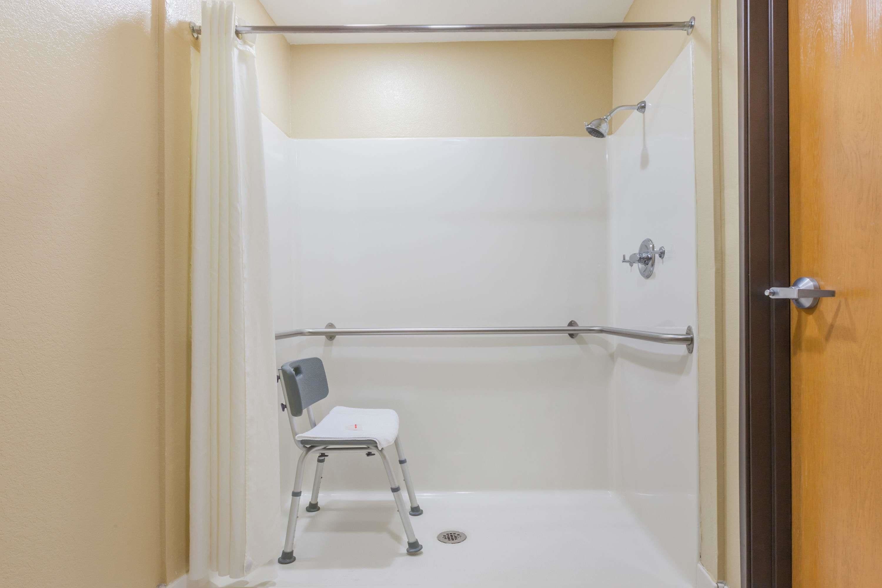 A small, enclosed shower area with a white chair and a grab bar.
