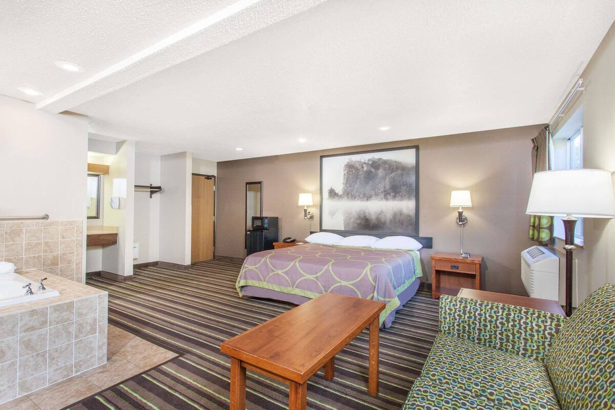 Une chambre d’hôtel comprenant un lit, un bureau, une chaise, une salle de bain avec baignoire et une grande fenêtre.