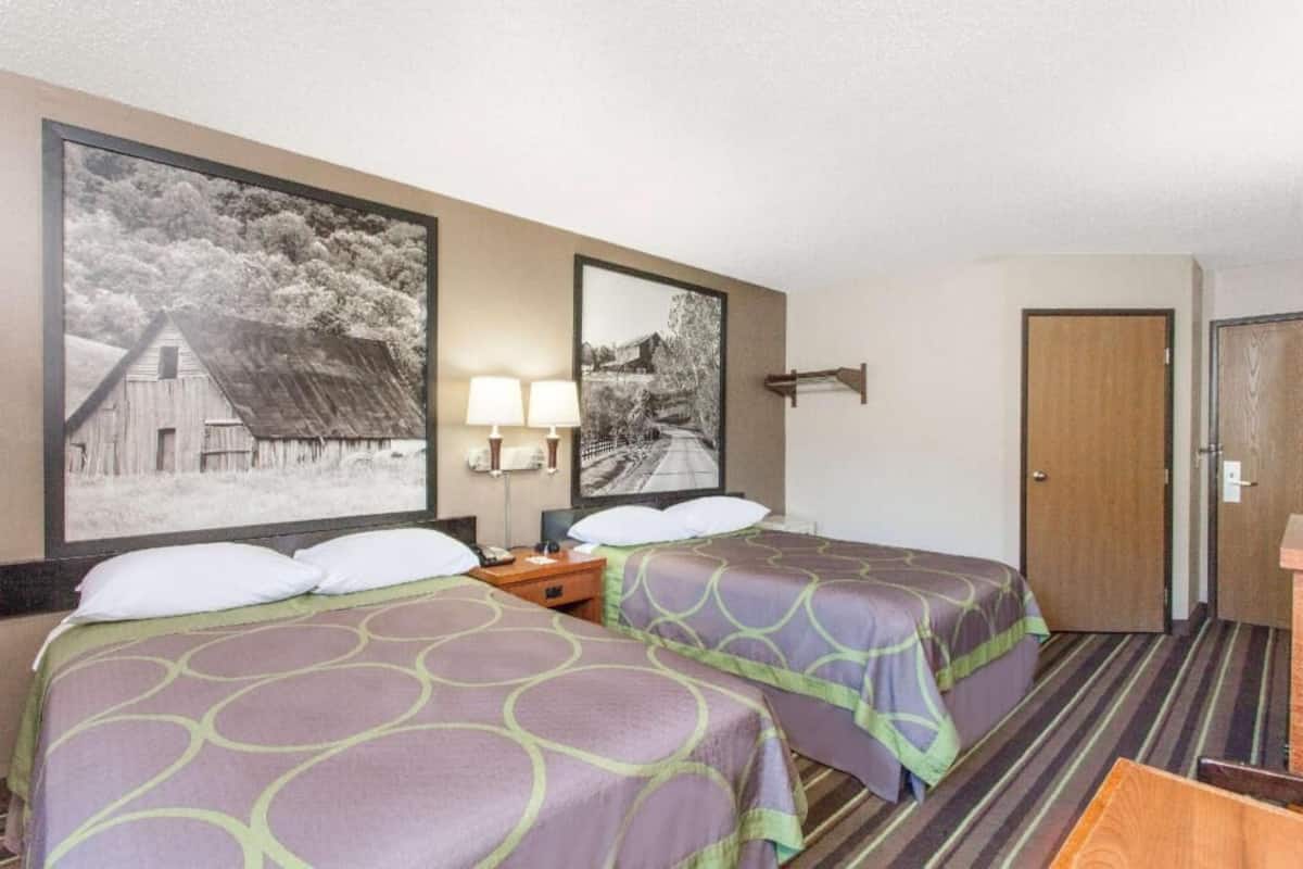 Une chambre d’hôtel avec deux lits, une table de chevet, une lampe et deux tableaux encadrés au mur.